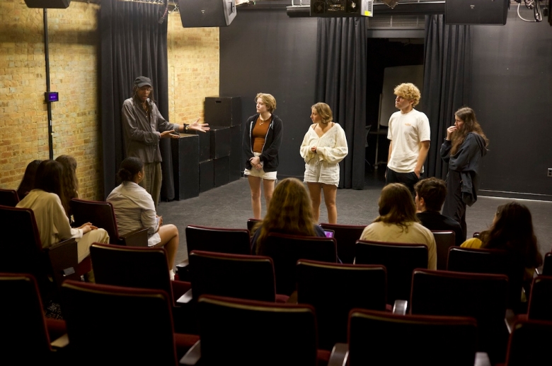 Dramatic Writing faculty William Electric Black stands on stage next to Dramatic Writing students in a Tisch class auditorium